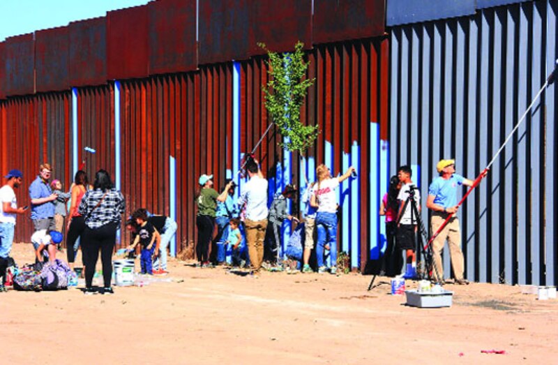 Un grupo de personas pinta un mural en la frontera entre Estados Unidos y México.