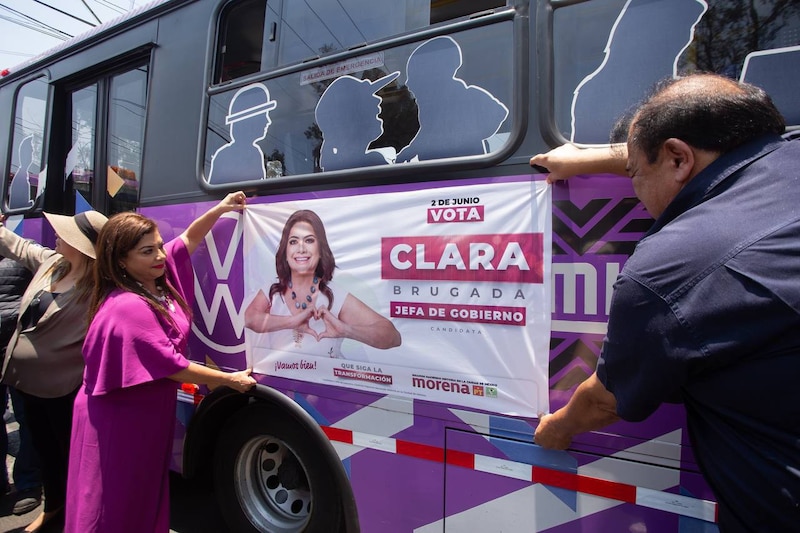 Clara Brugada, candidata de Morena a la jefatura de gobierno de la Ciudad de México, coloca un cartel en un autobús de campaña.