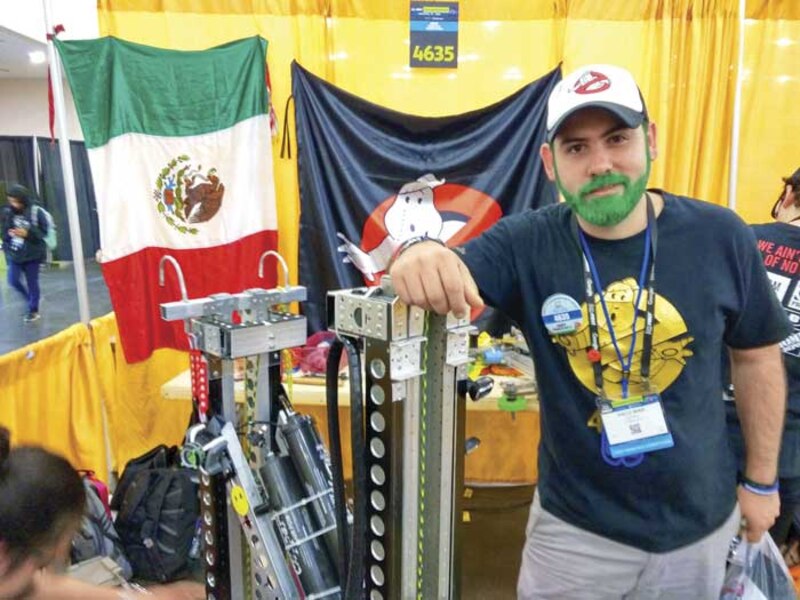 Un hombre con una barba verde y una camiseta de Los Cazafantasmas se encuentra frente a una bandera de México.